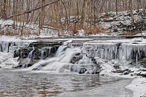 A frozen waterfall surrounded by icy rocks and bare trees in a winter landscape.