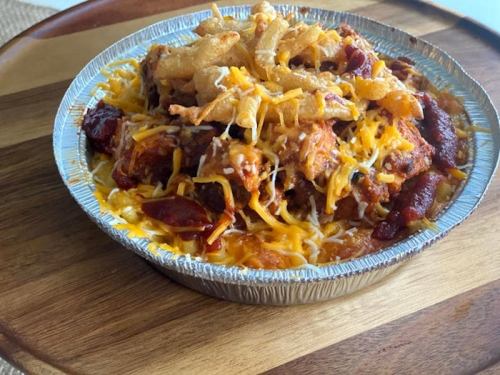 A silver pie dish filled with chili, cheese, and crispy onions, served on a wooden platter.