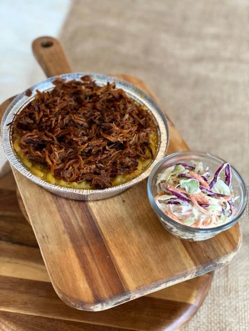 A dish of pulled meat in a foil tray next to a bowl of coleslaw, served on a wooden cutting board.
