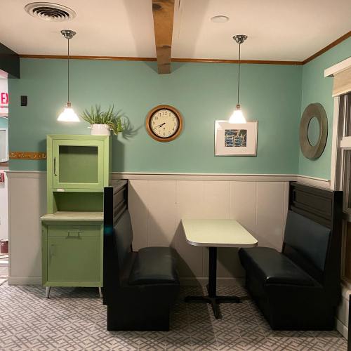 A cozy dining nook with green walls, a clock, and a small table surrounded by black booths and a green cabinet.