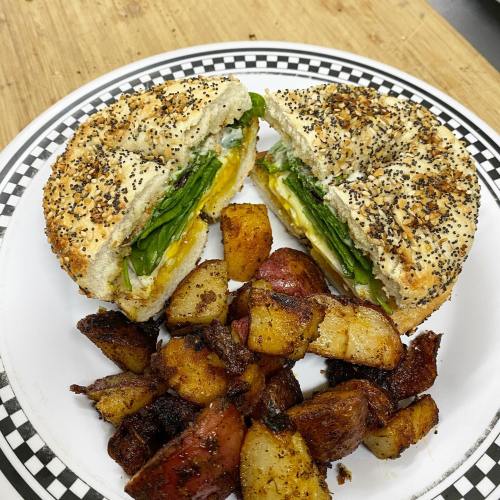 A poppy seed bagel sandwich filled with greens and egg, served with crispy roasted potatoes on the side.
