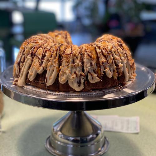 A beautifully decorated bundt cake topped with chocolate drizzle and nuts, displayed on a silver cake stand.