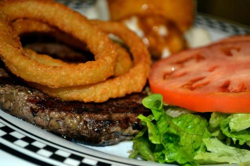 A juicy hamburger patty topped with crispy onion rings, fresh tomato slices, and lettuce on a checkered plate.