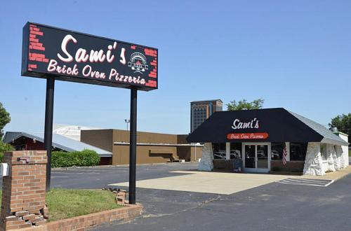 Exterior of Sami's Brick Oven Pizzeria, featuring a large sign and a modern building with a black roof.