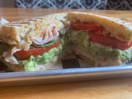 A close-up of a sandwich with turkey, tomatoes, and guacamole, cut in half on a wooden table.