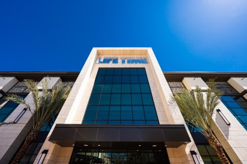 Exterior view of a modern building with large glass windows and palm trees, featuring the sign "LIFE TIME" on top.