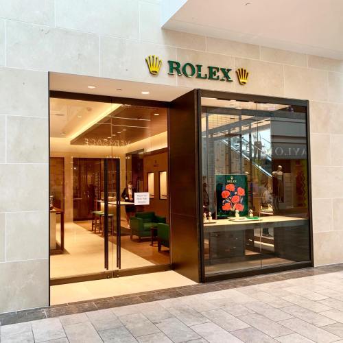 Exterior view of a Rolex store entrance, featuring a modern design and a display window with floral artwork.