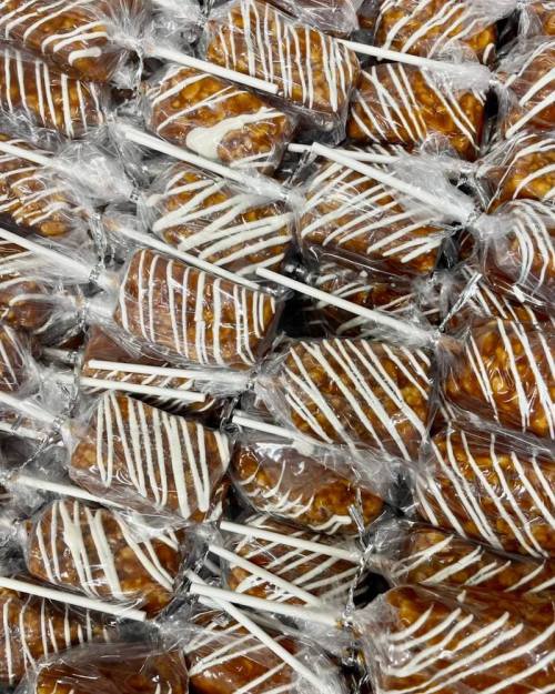 A close-up of individually wrapped caramel popcorn treats on sticks, drizzled with white icing.