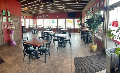 A spacious restaurant interior with tables, chairs, and large windows, featuring a warm color scheme and decorative plants.