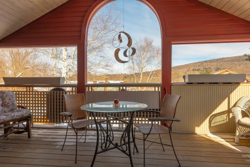 A cozy porch with a round table and chairs, featuring a scenic view through an arched window.