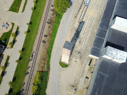 Aerial view of a railway track beside a building, with green spaces and pathways visible in the surrounding area.
