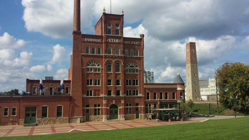 Historic brick building with a tall chimney, surrounded by green grass and a cloudy blue sky.