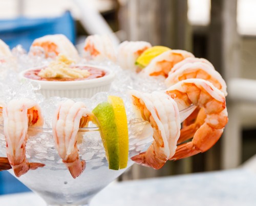 A chilled seafood platter featuring shrimp arranged on ice with lemon slices and a small bowl of cocktail sauce.