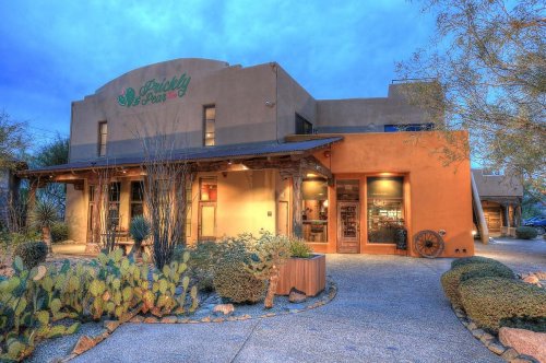 A southwestern-style building with a welcoming entrance, surrounded by desert landscaping and a blue sky.
