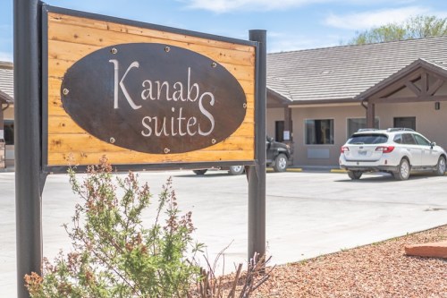 Sign for "Kanab Suites" in front of a building with parked cars and landscaping.