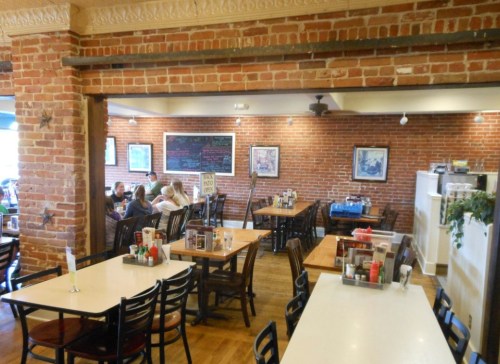Cozy restaurant interior with brick walls, wooden tables, and patrons dining in a casual atmosphere.