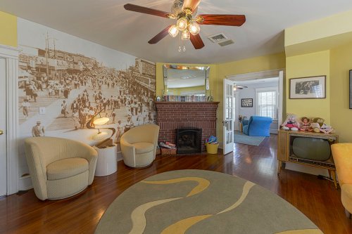 Cozy living room with yellow walls, a vintage fireplace, and a large mural, featuring two armchairs and a circular rug.