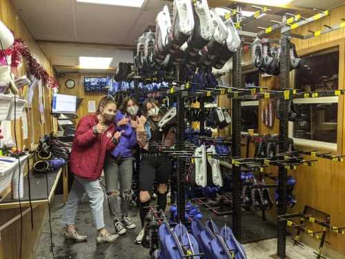 Three people pose with peace signs in a skate rental shop filled with skates on racks.