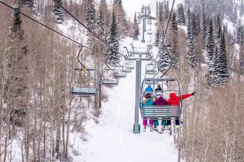 A group of skiers on a chairlift surrounded by snowy trees and mountains.