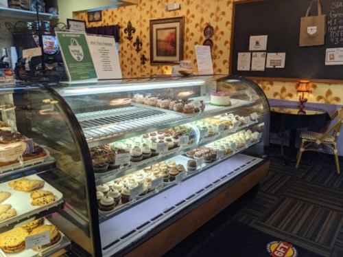 A display case filled with various colorful cupcakes and a cake in a cozy bakery setting.