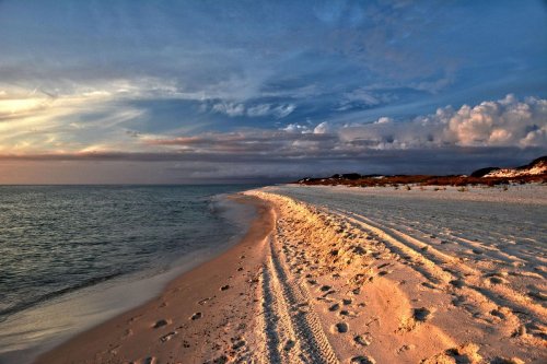 A serene beach at sunset, with soft sand, gentle waves, and a colorful sky filled with clouds.