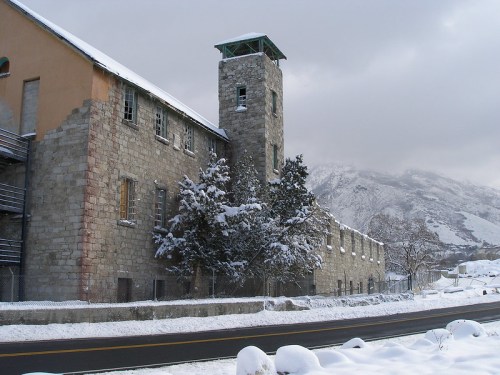 Abandoned stone building with a tower, surrounded by snow and mountains under a cloudy sky.