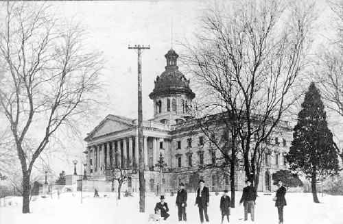 Historic black-and-white photo of a snow-covered building with people in winter attire standing in front.