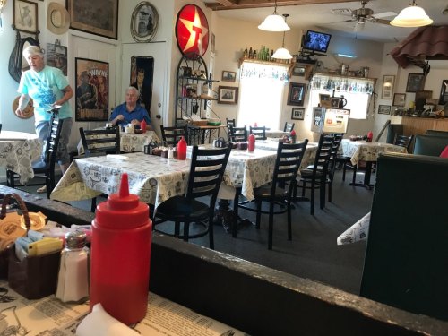 A cozy diner with empty tables, ketchup bottles on each, and a person walking in the background.