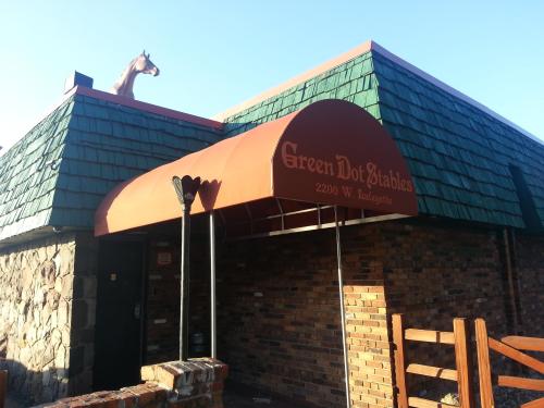 A building with a green shingle roof and an orange awning, featuring a horse statue on top. Sign reads "Green Dot Stables."