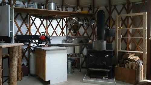 Cozy kitchen in a yurt, featuring a wood stove, shelves, and rustic decor with pots and utensils.