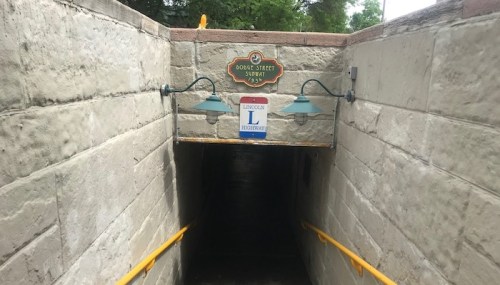 Entrance to a subway station with a sign for Dodge Street and Lincoln Highway, featuring yellow handrails and wall lights.
