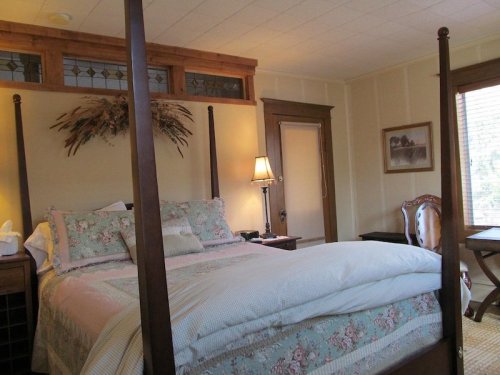 Cozy bedroom featuring a four-poster bed, soft bedding, and warm wooden accents, with a lamp and chair nearby.
