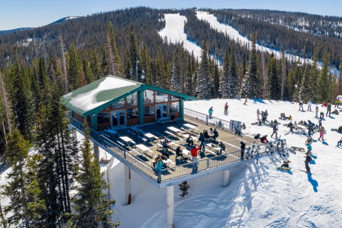 A ski lodge on a snowy mountain, surrounded by trees, with people enjoying the outdoor seating area.