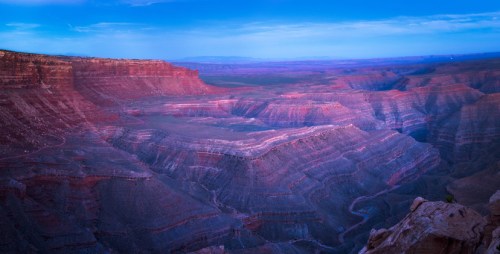 A panoramic view of the Grand Canyon at dusk, showcasing layered rock formations and a serene sky.