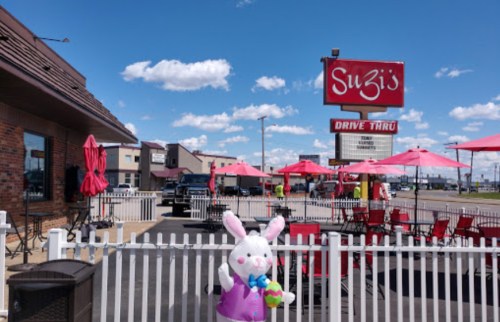 A drive-thru restaurant named Suzi's with outdoor seating, red umbrellas, and a decorative bunny figure in front.