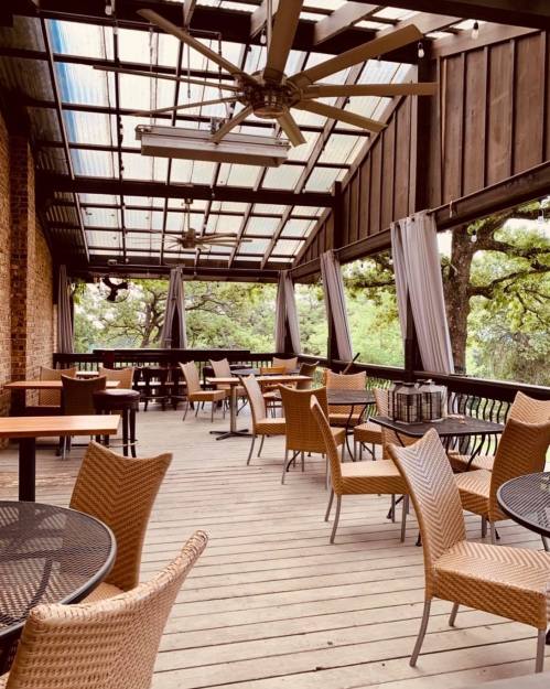A spacious outdoor dining area with wicker chairs and tables, featuring a covered roof and large ceiling fans.