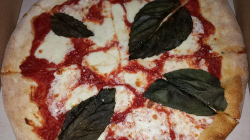A pizza topped with tomato sauce, mozzarella cheese, and large basil leaves, presented in a pizza box.