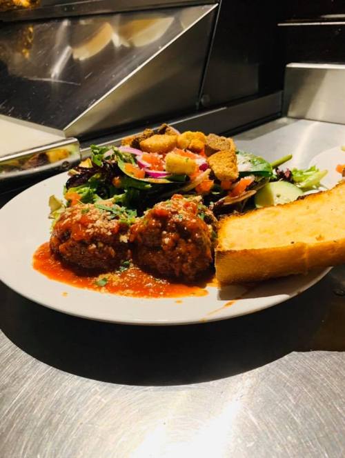 A plate of meatballs in marinara sauce, served with a side salad and a slice of bread.