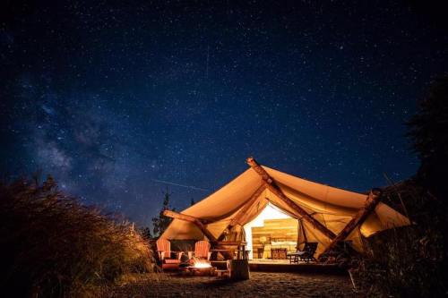 A cozy glamping tent under a starry night sky, with a warm glow from inside and a campfire nearby.