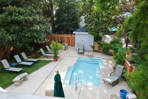 A backyard pool area with lounge chairs, a small pool, and greenery, surrounded by a wooden fence and a shed.