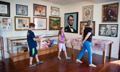 Two children and an adult explore a gallery filled with framed portraits and historical artifacts.