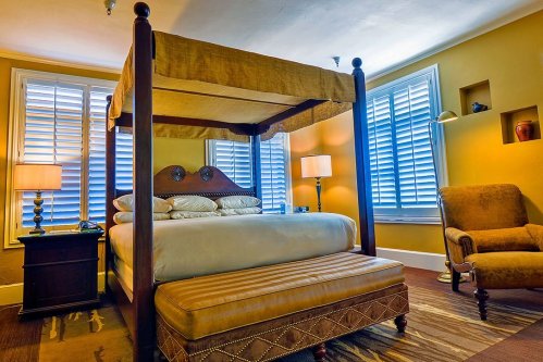A cozy bedroom featuring a four-poster bed, warm yellow walls, and a comfortable armchair by the window.