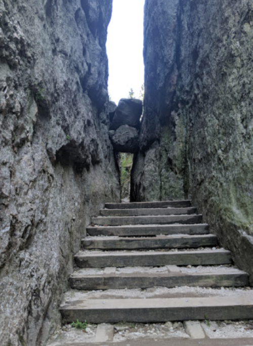 Narrow stone passageway with steps leading through a rocky crevice, surrounded by tall rock walls.