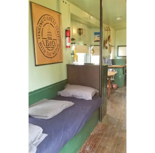 Cozy interior of a small room featuring a bed, wooden floor, and a dining area with a nautical-themed wall decoration.