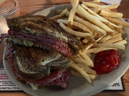 A plate with a stacked sandwich filled with meat and pickles, served with golden fries and a side of ketchup.