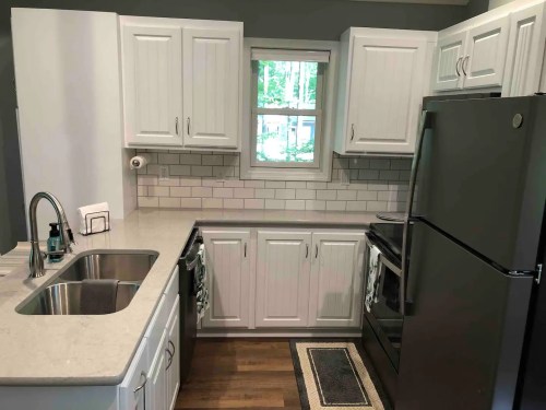 Modern kitchen with white cabinets, stainless steel appliances, and a window overlooking greenery.