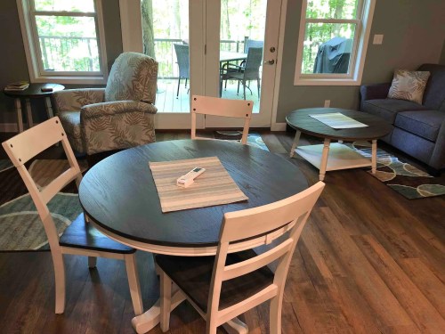Cozy living space featuring a round dining table, chairs, and a sofa, with large windows overlooking a deck.