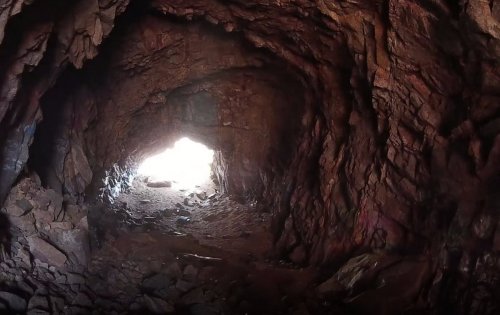 View from inside a cave, showing a bright light at the entrance and rocky walls surrounding the dark interior.