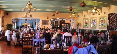 A vibrant restaurant interior filled with diners, featuring colorful stained glass windows and decorative lighting.