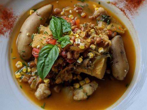 A colorful bowl of stew with chicken, corn, vegetables, and herbs, garnished with fresh basil.